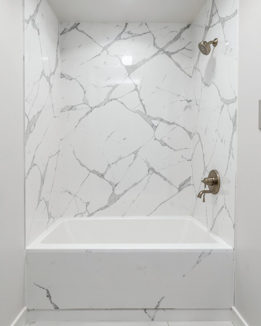 Bathroom tub surrounded by warm stone-look acrylic wall panels with brass fixtures