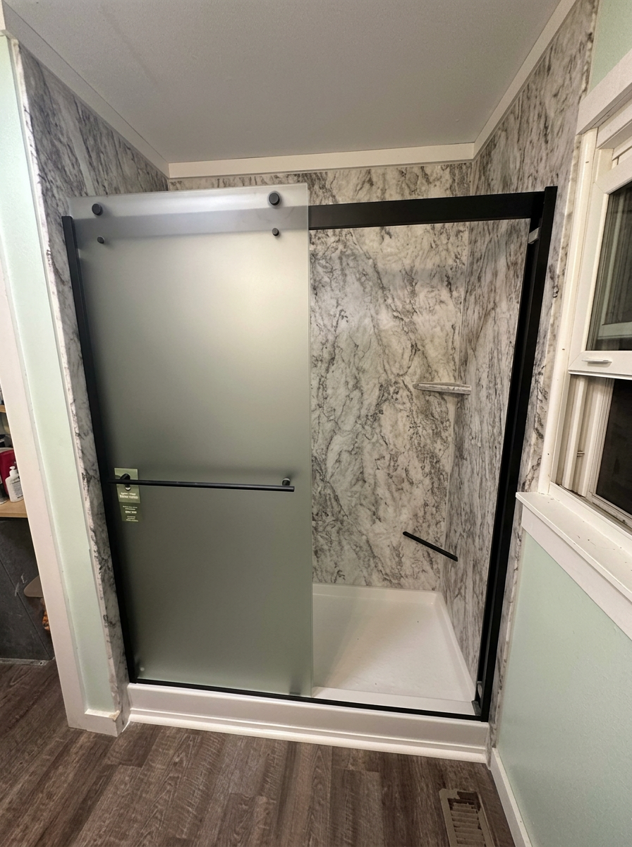Completed gray marble-look shower with matte-black framed frosted sliding glass door, white shower base, and adjacent window
