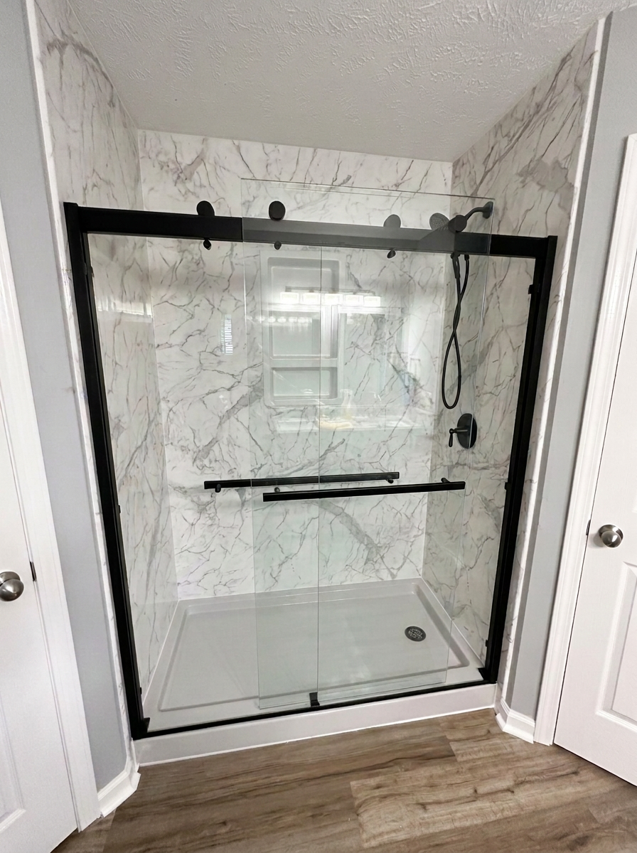 Completed white marble-look acrylic shower with black-framed sliding glass door and wood-look flooring