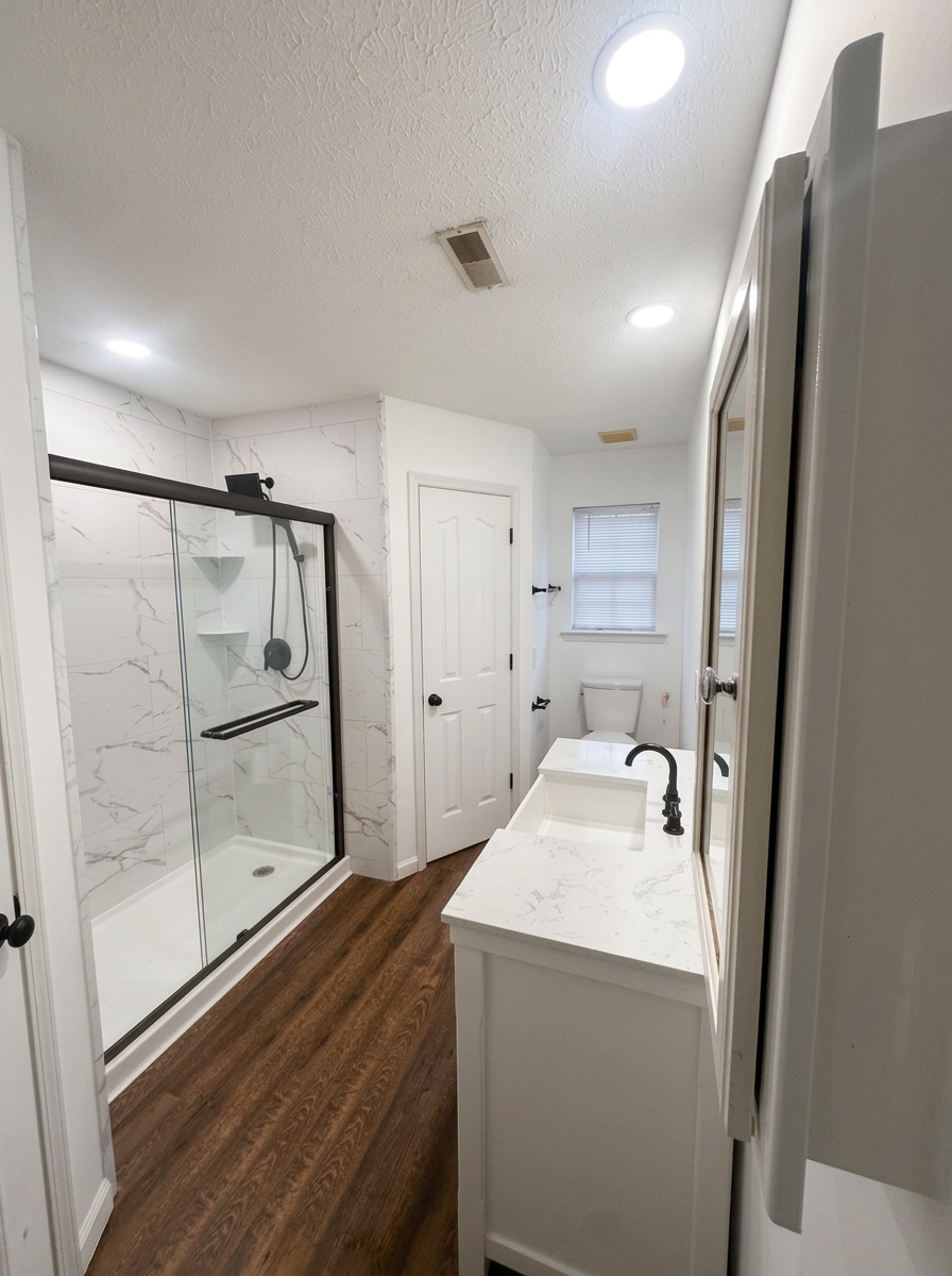 Completed white marble-look shower and bathroom with black-framed sliding glass door, white vanity, and wood-look flooring